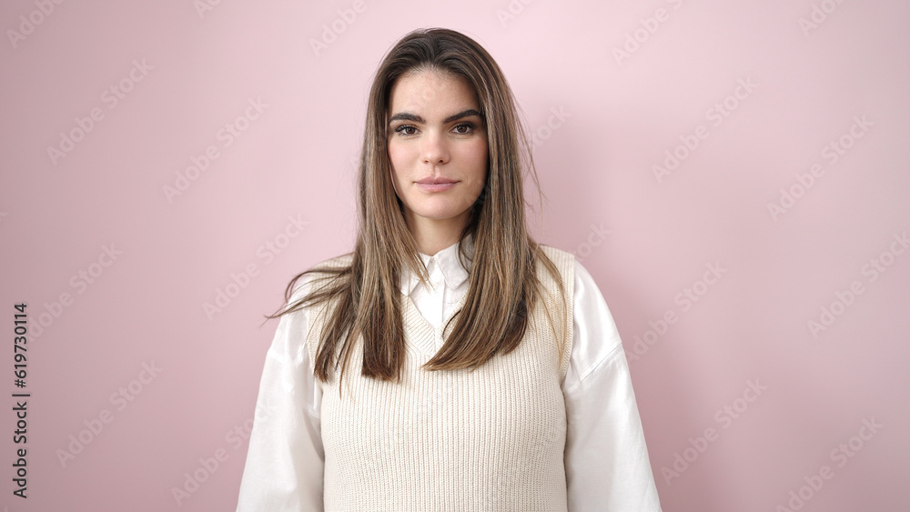 Young beautiful hispanic woman standing with serious expression over isolated pink background