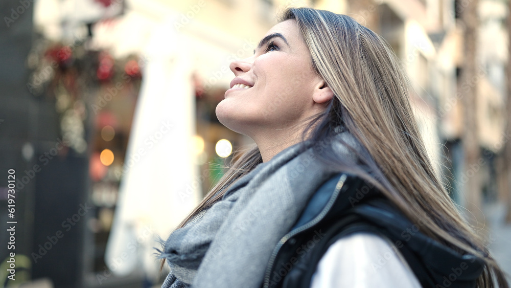 Young beautiful hispanic woman smiling looking up at street