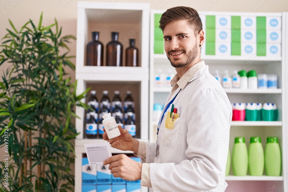 Young caucasian man pharmacist reading prescription holding pills bottle at pharmacy