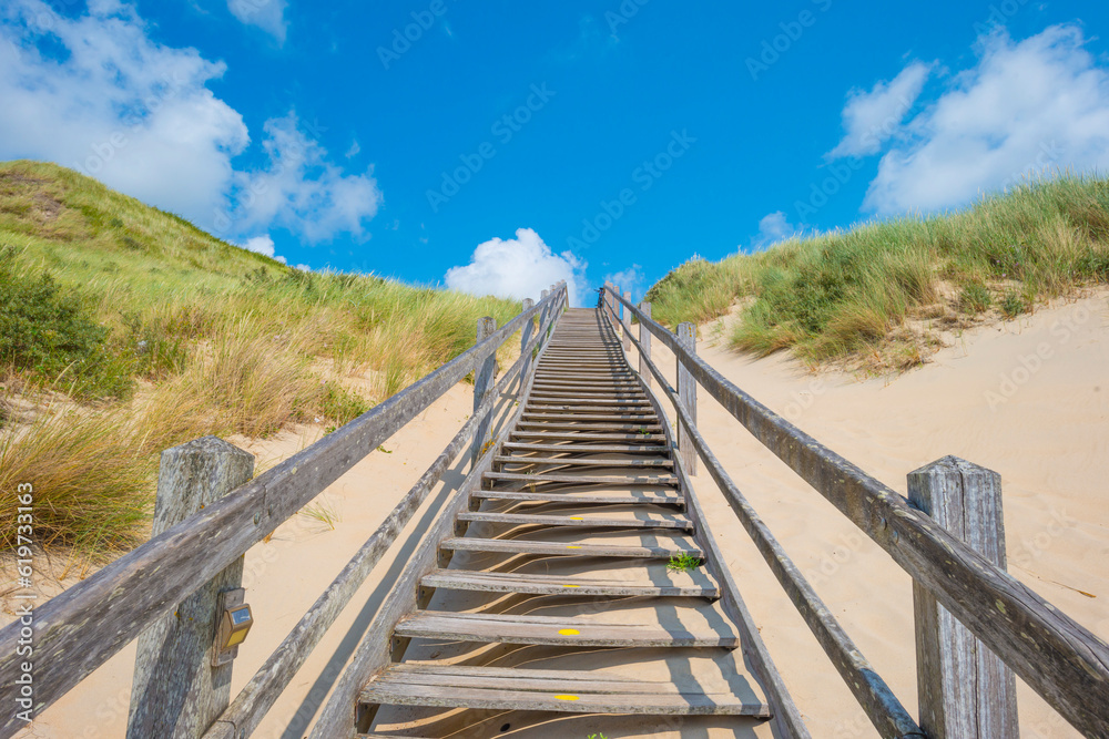 Sand beach along a sea under a dark blue cloudy sky in bright sunlight in summer, Zeeland, the Netherlands, June, 2023