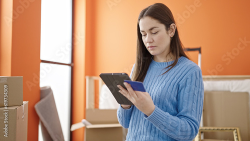 Young caucasian woman shopping with touchpad and credit card at new home