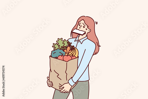 Woman carries shopping bag and holds phone in mouth after returning from grocery market with organic food. Girl bought lot of healthy food and is trying to bring organic vegetables and fruits on own