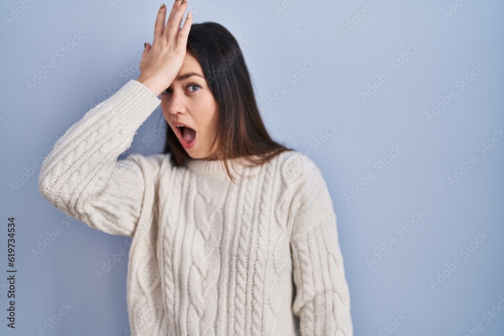 Young brunette woman standing over blue background surprised with hand on head for mistake, remember error. forgot, bad memory concept. Young brunette woman standing over blue background surprised with hand on head for mistake, remember error. forgot, bad memory concept.