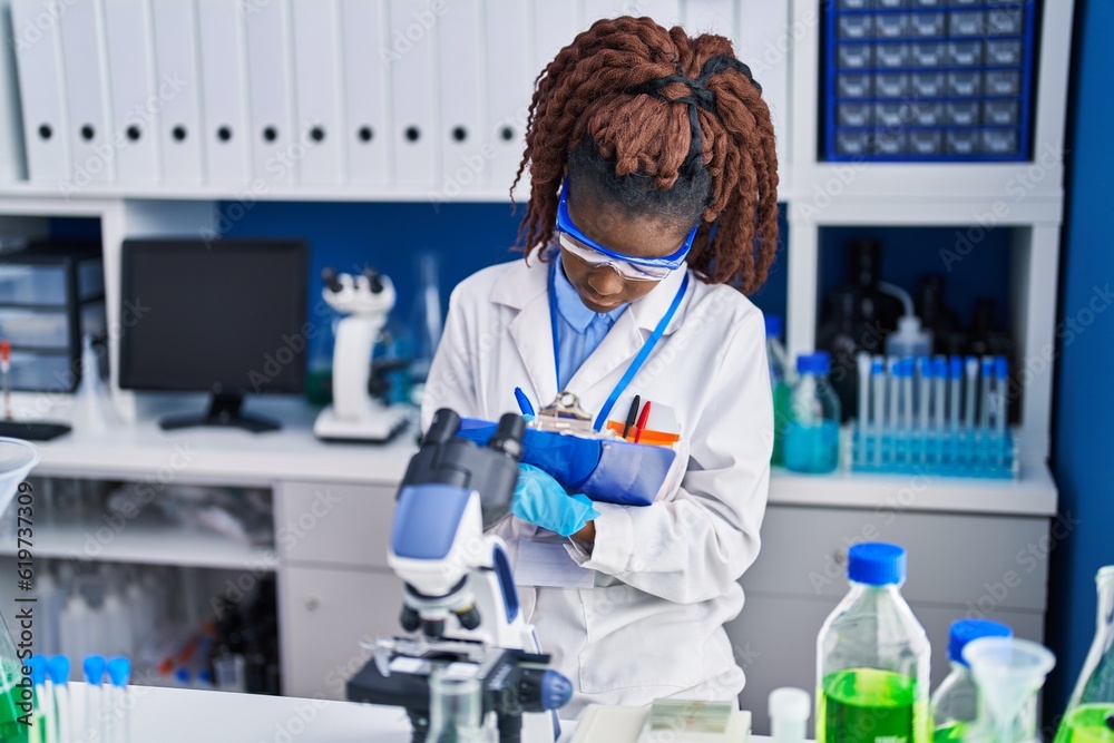 African american woman scientist writing report working at laboratory African american woman scientist writing report working at laboratory