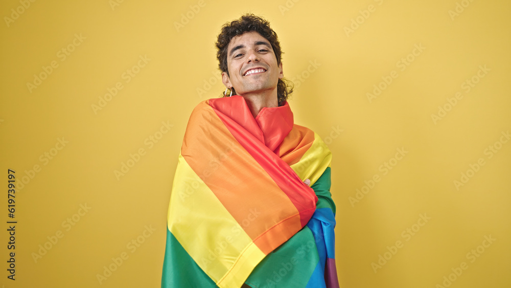 Young hispanic man smiling confident wearing rainbow flag over isolated yellow background Young hispanic man smiling confident wearing rainbow flag over isolated yellow background