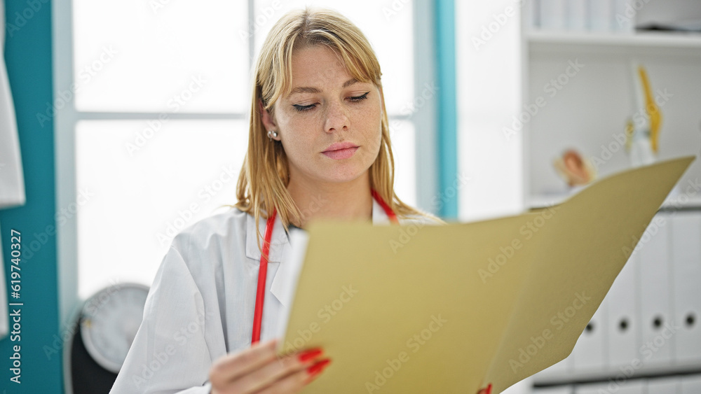 Young blonde woman doctor reading medical report at clinic Young blonde woman doctor reading medical report at clinic