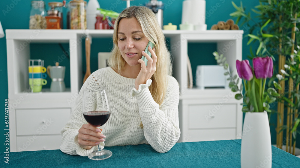 Young blonde woman drinking glass of wine talking on smartphone at dinning room Young blonde woman drinking glass of wine talking on smartphone at dinning room