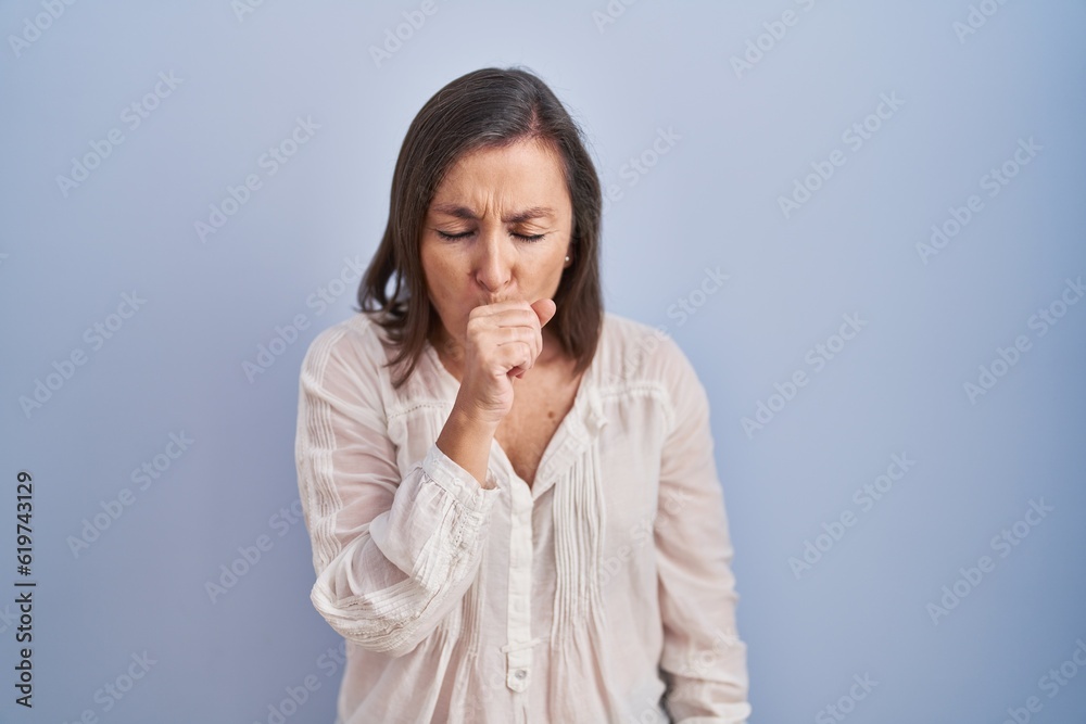 Middle age hispanic woman standing over blue background feeling unwell and coughing as symptom for cold or bronchitis. health care concept. Middle age hispanic woman standing over blue background feeling unwell and coughing as symptom for cold or bronchitis. health care concept.
