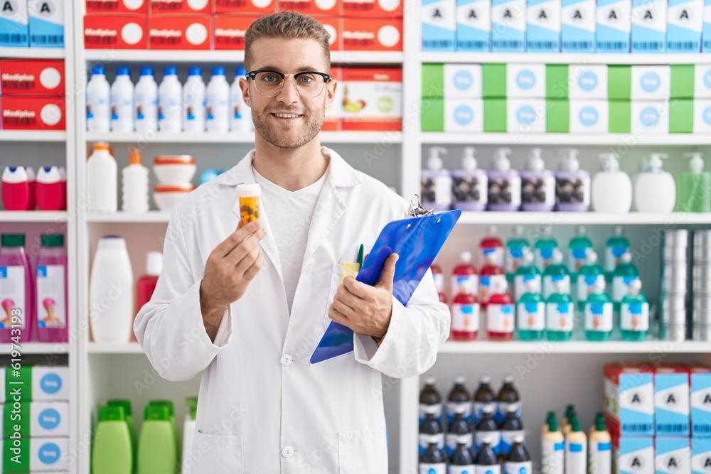 Young caucasian man working at pharmacy drugstore holding pills smiling with a happy and cool smile on face. showing teeth.
