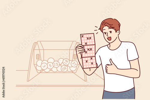 Man won bingo lottery happily demonstrates winning ticket and stands near transparent box with balls. Casino winner jackpot winner showing thumbs up feeling joyful in anticipation of big cash prize