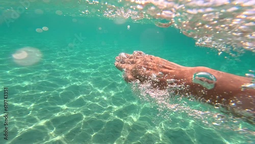 Man swims freestyle in the sea, underwater footage, strong hands goes through the seawater making lots of bubbles. Point of view shot, slow motion. Beautiful day and turquoise Aegean sea in Greece