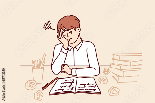 Thinking schoolboy does homework sitting at table with books and workbook after exhausting classes with tutor. Tired schoolboy from elementary school needs rest to replenish strength