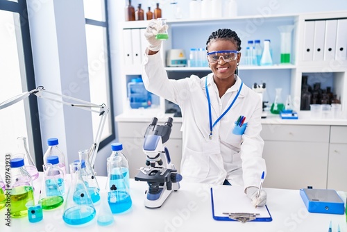 African american woman scientist holding test tube writing report at laboratory