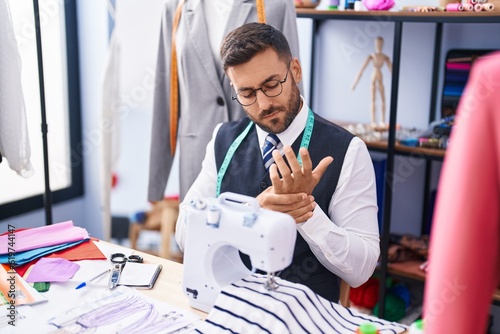 Young hispanic man tailor stressed using sewing machine at tailor shop