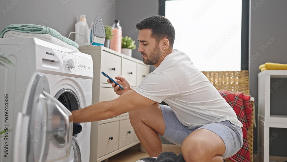 Young hispanic man washing clothes using smartphone at laundry room Young hispanic man washing clothes using smartphone at laundry room
