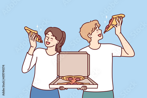 Man and woman eat pizza holding box of italian snacks and satisfying hunger together with fast food delivered from restaurant. Couple ordering pizza in pizzeria having lunch with pleasure