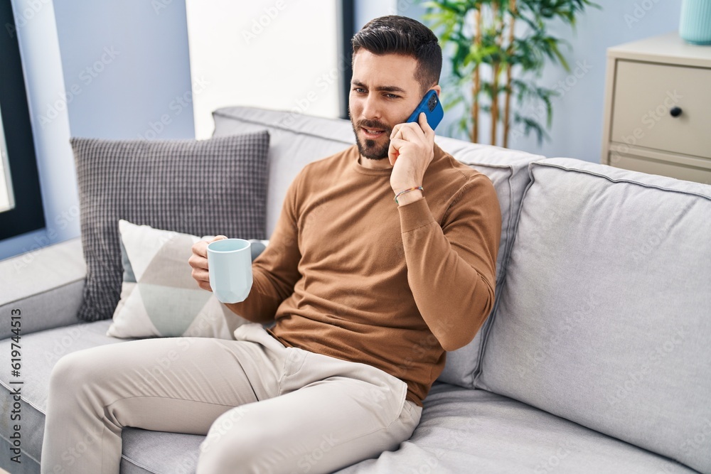 Young hispanic man drinking coffee and talking on the smartphone at home Young hispanic man drinking coffee and talking on the smartphone at home