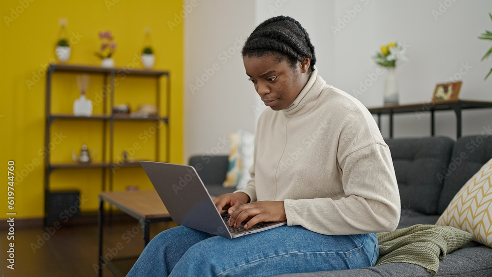 African american woman using laptop sitting on sofa at home African american woman using laptop sitting on sofa at home