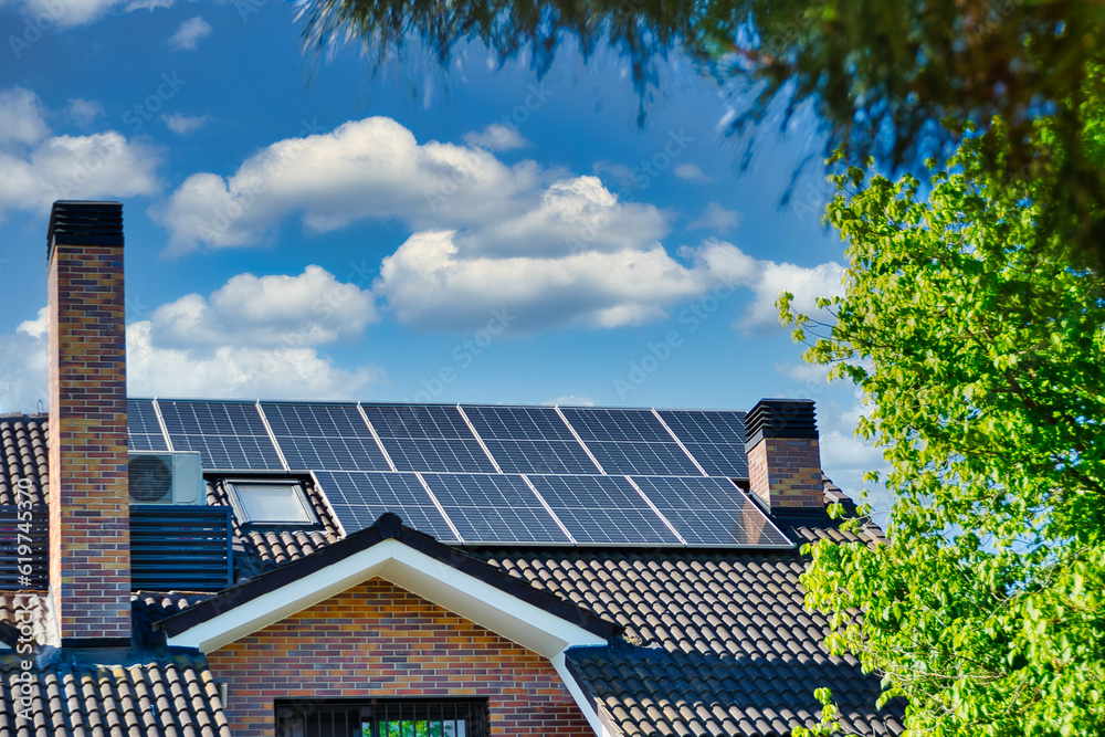 Fototapeta premium Roofs with solar panels and clouds on background blue sky.