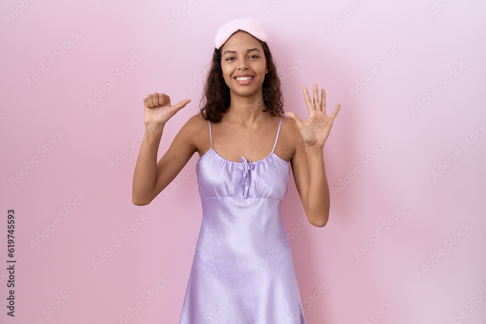 Young hispanic woman wearing sleep mask and nightgown showing and pointing up with fingers number six while smiling confident and happy. Young hispanic woman wearing sleep mask and nightgown showing and pointing up with fingers number six while smiling confident and happy.
