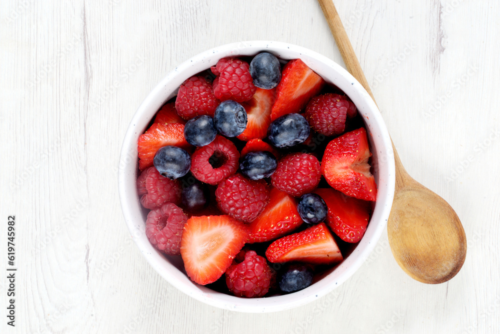 White bowl with red fruits on white wooden board White bowl with red fruits on white wooden board