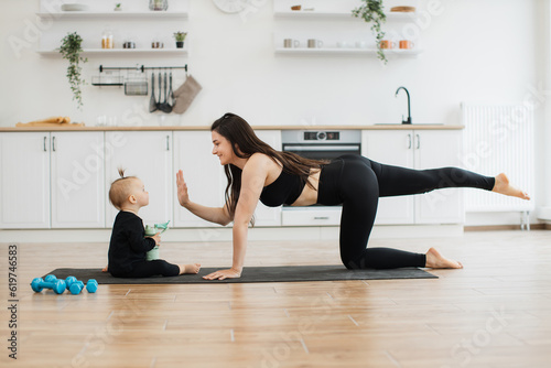 Φωτογραφία Side view of beautiful woman giving high five to cute baby girl while achieving yoga position indoors