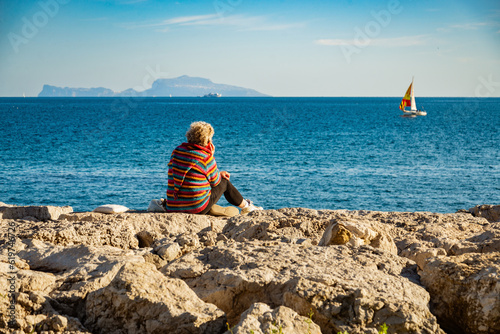Woman looks at the Meditarrean sea sitting on rocks photo