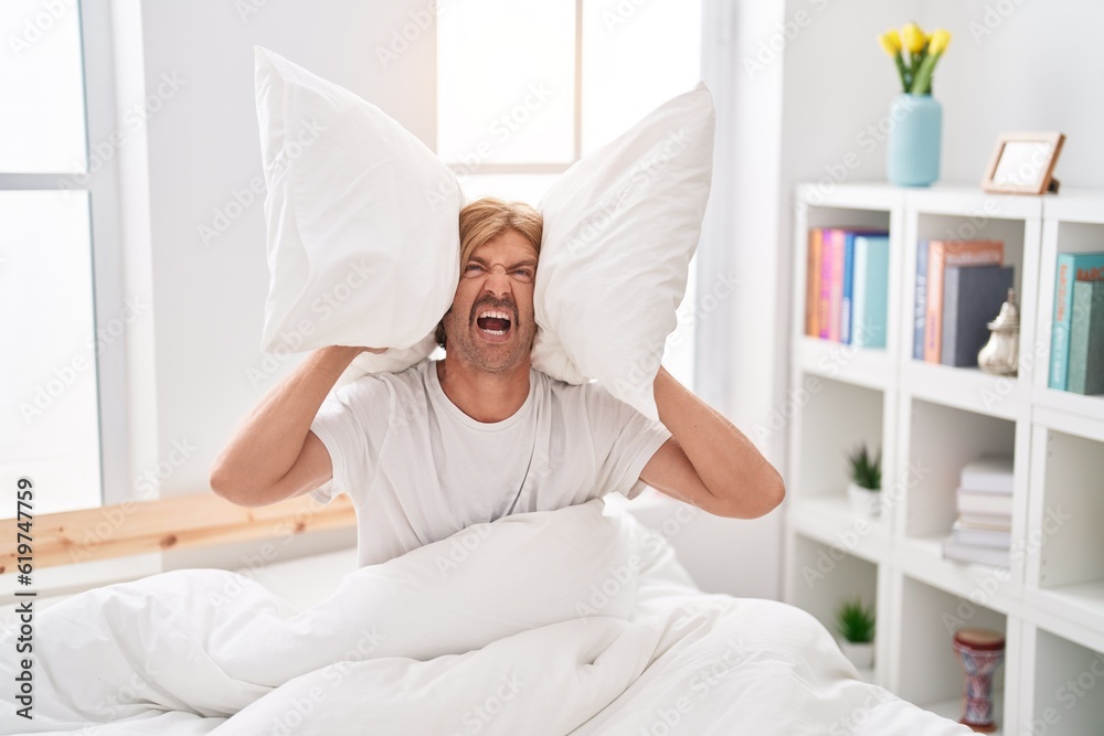 Young blond man covering ears for noise at bedroom Young blond man covering ears for noise at bedroom