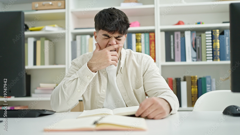 Young hispanic man student tired reading book sitting on table at library university Young hispanic man student tired reading book sitting on table at library university
