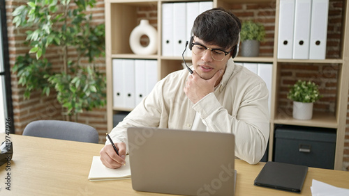 Young hispanic man business worker having online meeting writing notes at office