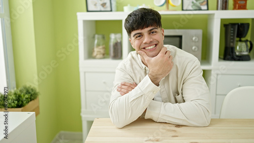 Young hispanic man sitting on table smiling confident at dinning room