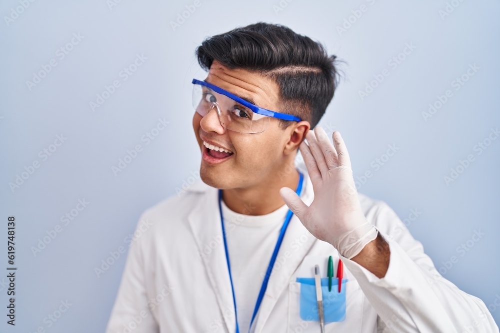 Hispanic man working as scientist smiling with hand over ear listening an hearing to rumor or gossip. deafness concept. Hispanic man working as scientist smiling with hand over ear listening an hearing to rumor or gossip. deafness concept.