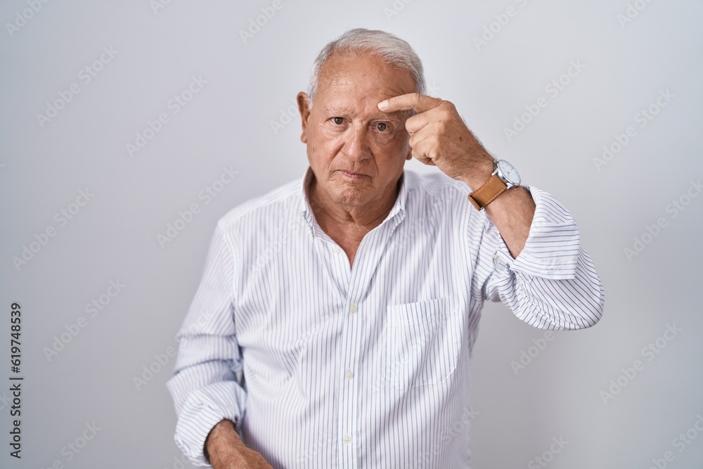 Senior man with grey hair standing over isolated background pointing unhappy to pimple on forehead, ugly infection of blackhead. acne and skin problem Senior man with grey hair standing over isolated background pointing unhappy to pimple on forehead, ugly infection of blackhead. acne and skin problem