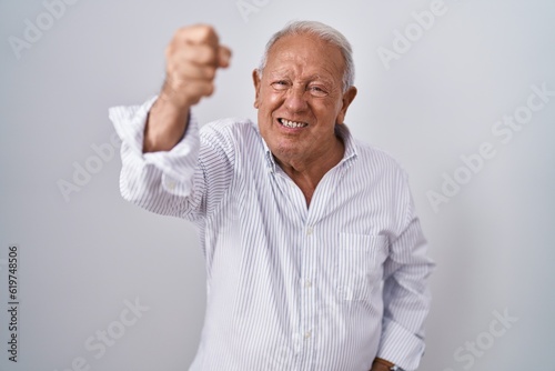 Senior man with grey hair standing over isolated background angry and mad raising fist frustrated and furious while shouting with anger. rage and aggressive concept.