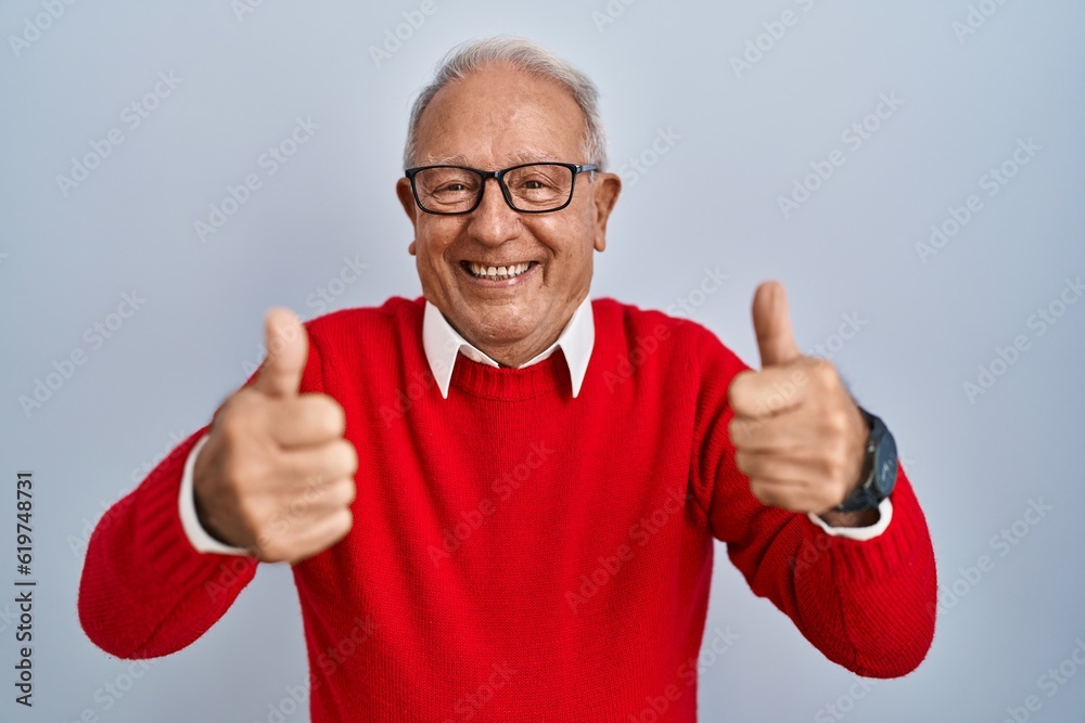 Senior man with grey hair standing over isolated background success sign doing positive gesture with hand, thumbs up smiling and happy. cheerful expression and winner gesture. Senior man with grey hair standing over isolated background success sign doing positive gesture with hand, thumbs up smiling and happy. cheerful expression and winner gesture.