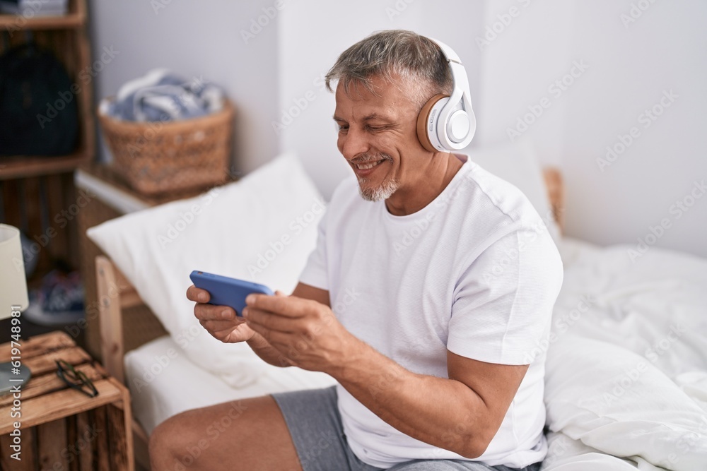 Middle age grey-haired man watching video on smartphone sitting on bed at bedroom Middle age grey-haired man watching video on smartphone sitting on bed at bedroom