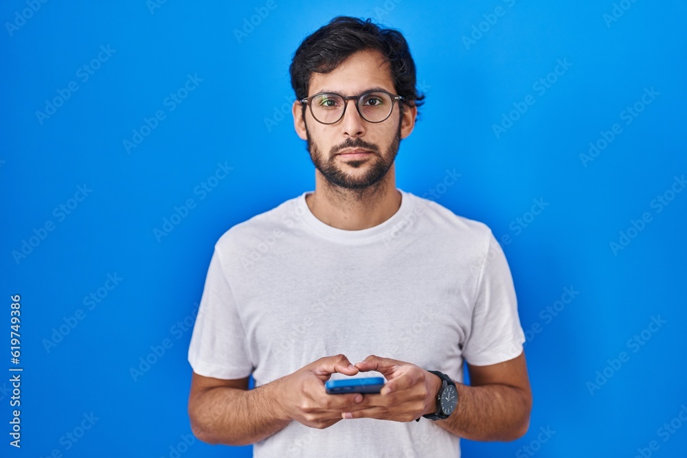 Handsome latin man using smartphone typing message relaxed with serious expression on face. simple and natural looking at the camera. Handsome latin man using smartphone typing message relaxed with serious expression on face. simple and natural looking at the camera.