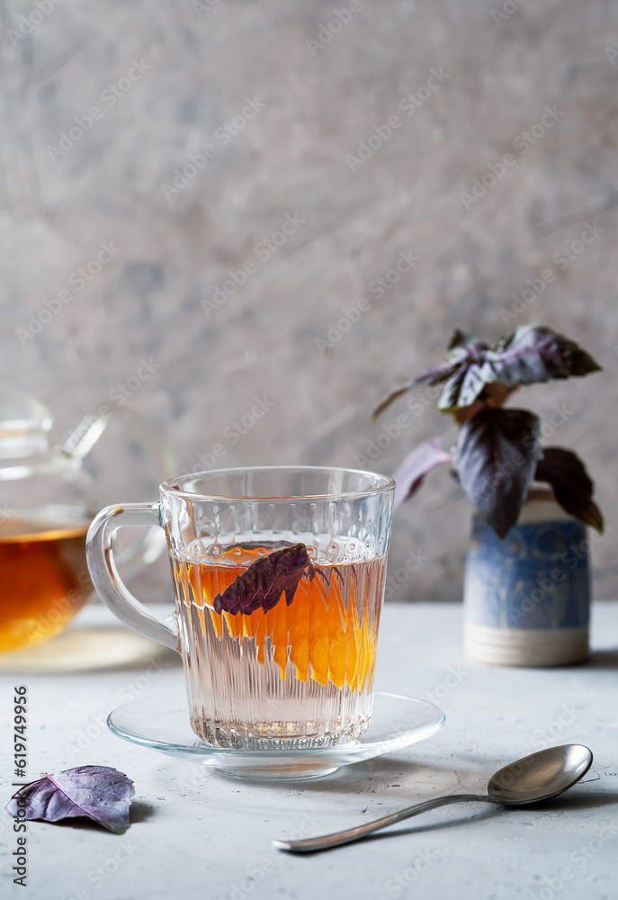 Healthy and immune boosty purple basil tea in a glass mugs with slice of orange and fresh leaves backside. Grey concrete background, vertical banner with space for text Healthy and immune boosty purple basil tea in a glass mugs with slice of orange and fresh leaves backside. Grey concrete background, vertical banner with space for text
