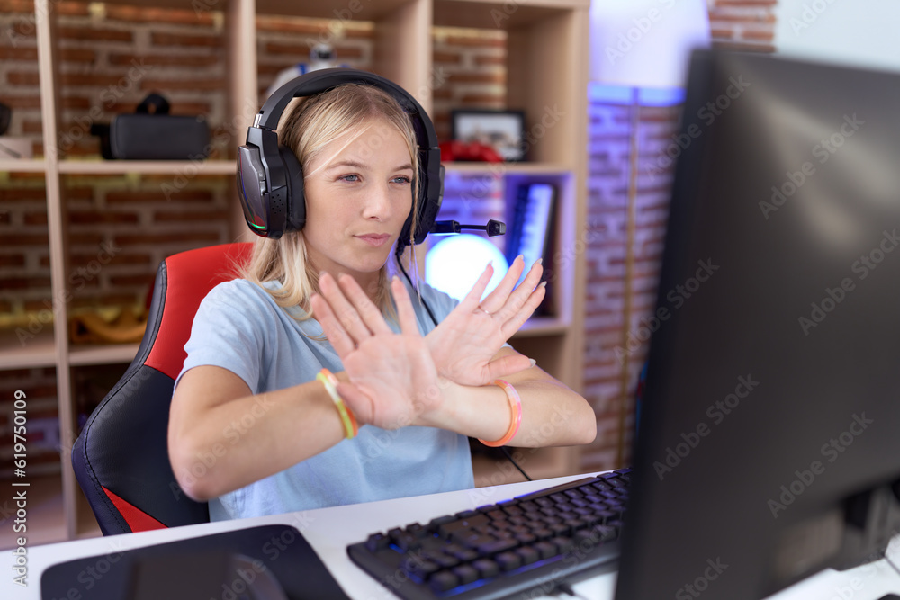 Young caucasian woman playing video games wearing headphones rejection expression crossing arms and palms doing negative sign, angry face Young caucasian woman playing video games wearing headphones rejection expression crossing arms and palms doing negative sign, angry face
