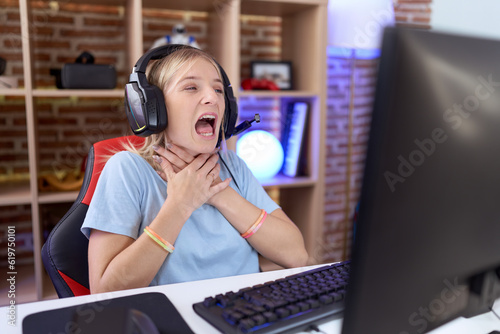 Young caucasian woman playing video games wearing headphones shouting suffocate because painful strangle. health problem. asphyxiate and suicide concept. photo