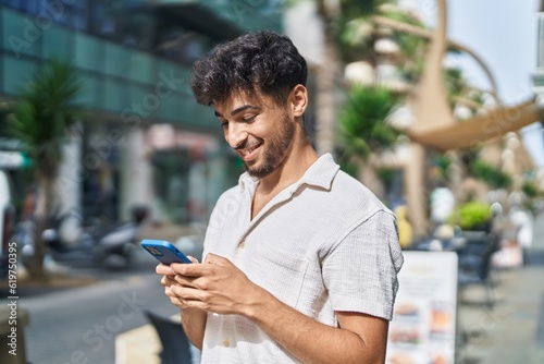 Young arab man smiling confident using smartphone at street