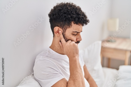 Young arab man suffering for ear pain sitting on bed at bedroom photo