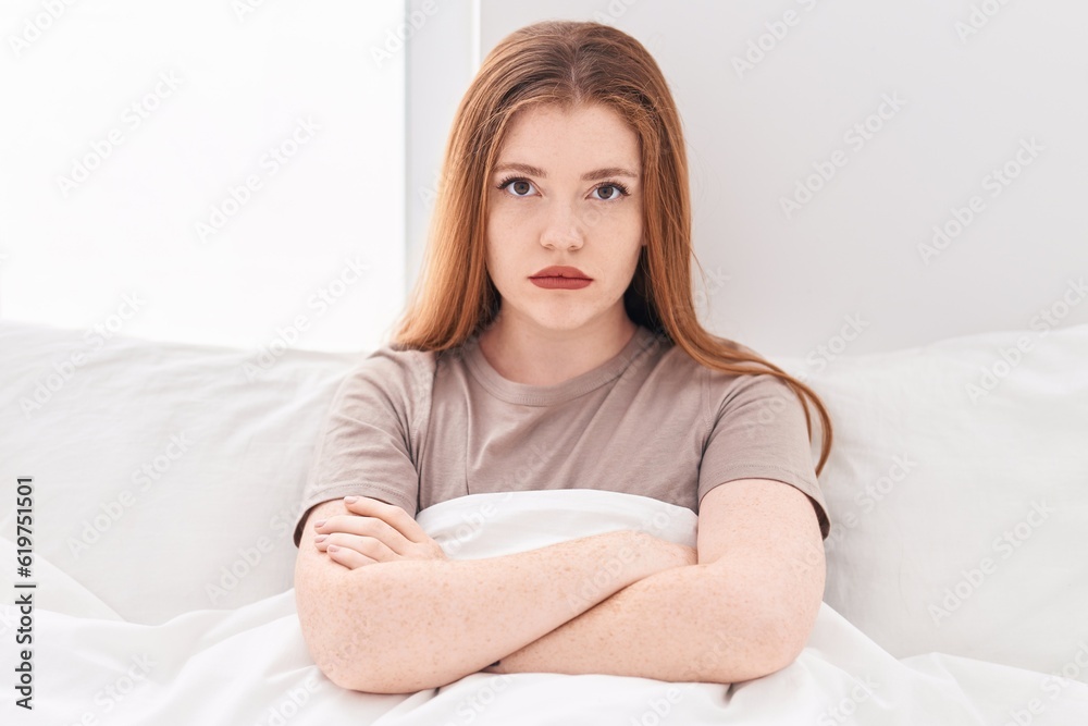 Young redhead woman sitting on bed with unhappy expression and arms crossed gesture at bedroom Young redhead woman sitting on bed with unhappy expression and arms crossed gesture at bedroom