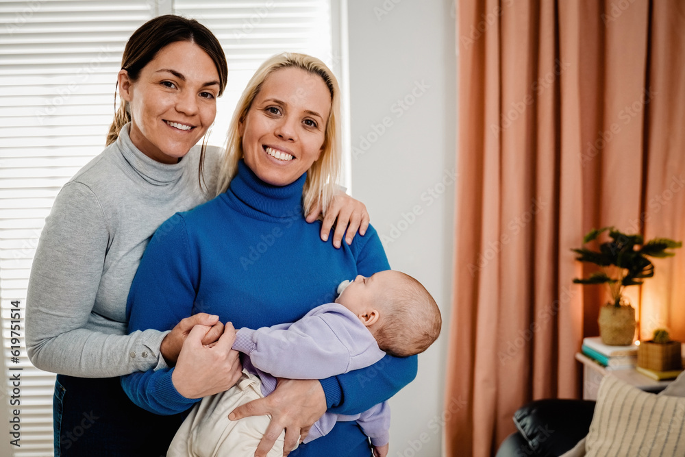 Fototapeta premium Gay lesbian couple and newborn baby having tender moment indoors at home - Lgbt family concept - Focus on infant head