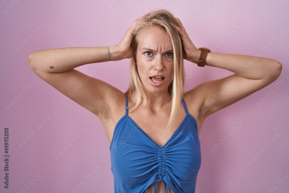 Young caucasian woman standing over pink background crazy and scared with hands on head, afraid and surprised of shock with open mouth Young caucasian woman standing over pink background crazy and scared with hands on head, afraid and surprised of shock with open mouth
