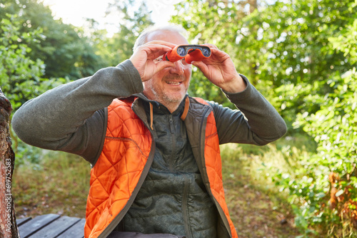 Senior man bird watching with binoculars in autumn forest