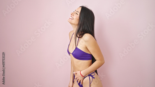 Young beautiful hispanic woman tourist smiling confident wearing bikini over isolated pink background