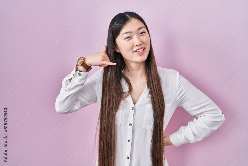 Chinese young woman standing over pink background smiling doing phone gesture with hand and fingers like talking on the telephone. communicating concepts. Chinese young woman standing over pink background smiling doing phone gesture with hand and fingers like talking on the telephone. communicating concepts.