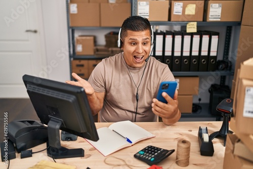 Hispanic young man working at small business ecommerce on video call celebrating achievement with happy smile and winner expression with raised hand
