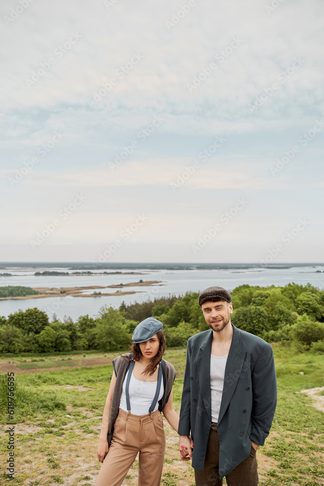 Smiling bearded man in vintage-inspired outfit holding hand of brunette ...